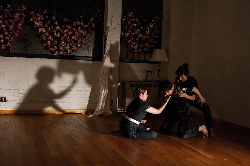 Three dancers dressed in black intertwine their bodies in the shadows